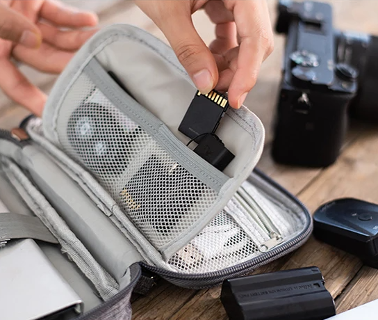 Close-up of a Pro-Travel Tech Organizer Pouch being used to store an SD card, with a camera and batteries in the background.